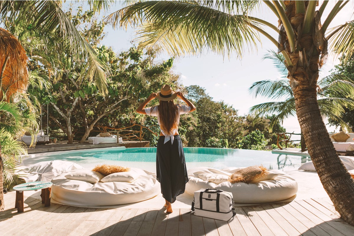 women overlooking pool on vacation with weekender bag